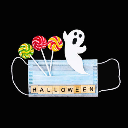 Cut out paper ghost, colorful lollipops, medical mask and word Halloween on black. Halloween background decor holiday concept, Square formatの写真素材