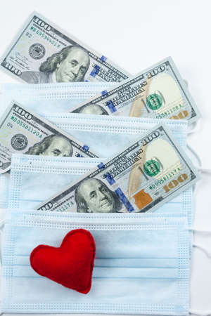 Red heart, medical masks and dollars.Helping poor countries with money and masks.Financial crisis due to coronavirus.Cash payments to doctors.Expensive hospital services. Medical research.の写真素材
