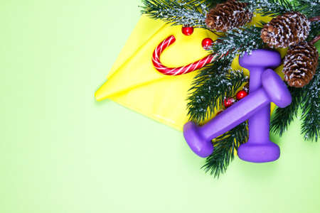 Christmas fitness. Healthy and active lifestyles greeting card concept. Purple dumbbells, yellow rubber band, candy and fir-tree on greenの写真素材