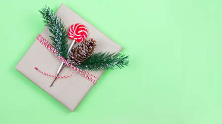 Christmas gift box wrapped in brown craft paper with corn, fir-tree and candy on green background. New Year and Christmas concept. Eco package. Focus on corn. Bannerの写真素材