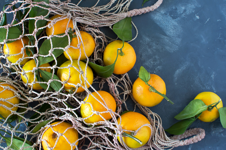 Tangerines with leaves close-up on a blue background in a bag grid. Horizontal photo.の写真素材