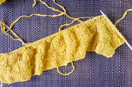 Close-up of the knitted product on the spokes. Yellow woolen product on a dark background.