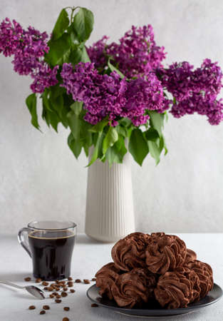 coffee marshmallows on a light background in a plate, in the background - a cup of coffee, lilac sprigs.の写真素材