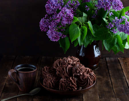 coffee marshmallow on a wooden background in a plate, in the background - a cup of coffee, lilac branches.の写真素材