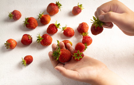 A child's hand holding strawberries on a light background, a plate with strawberries. The concept of...