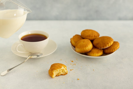 Delicious snack: a cup of black tea with milk and a plate of cookies on a gray background.
