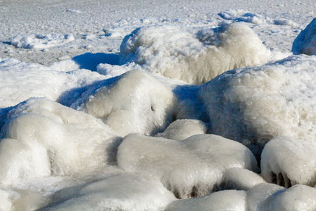 Close-up of the icy seashore, frozen waves, rocks and sun glare on the ice