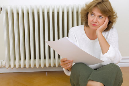 Mature woman with short gray hair, wearing a cozy sweater, is sitting indoors, looking thoughtfully at documents, reflecting on important decisions in a warm and inviting environmentの素材