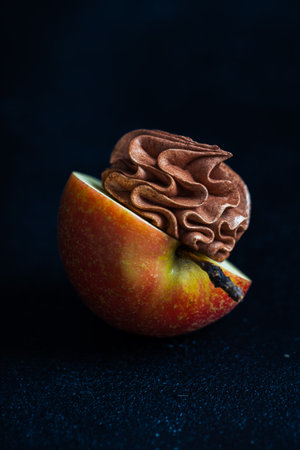 Half of a vibrant apple topped with luscious chocolate mousse, artistically displayed on a dark surface, highlighting the contrast of textures and flavorsの写真素材