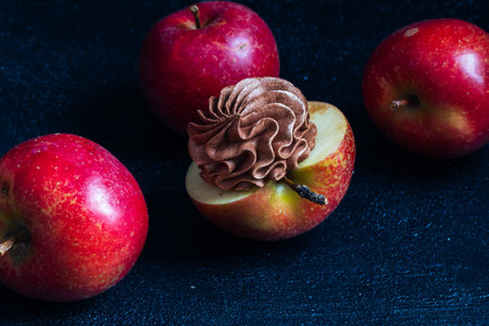 Vibrant red apples are beautifully arranged, featuring a sliced apple topped with rich chocolate swirl, highlighting the contrast of colors and textures in a culinary displayの写真素材
