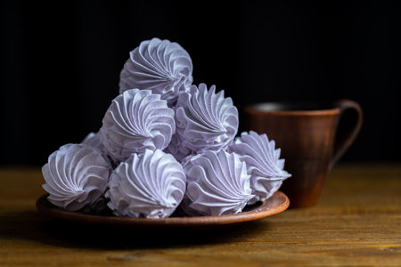 Homemade lavender zephyr beautifully displayed on a wooden plate, accompanied by a warm cup, creating a cozy and inviting atmosphere for dessert loversの写真素材