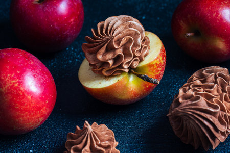 Vibrant red apples are artistically arranged, featuring a halved apple topped with luscious chocolate frosting, creating an enticing dessert scene with rich texturesの写真素材