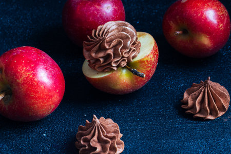 Red apples are beautifully presented with a chocolate cream topping, creating an enticing dessert scene with whole apples scattered on a dark textured backgroundの写真素材