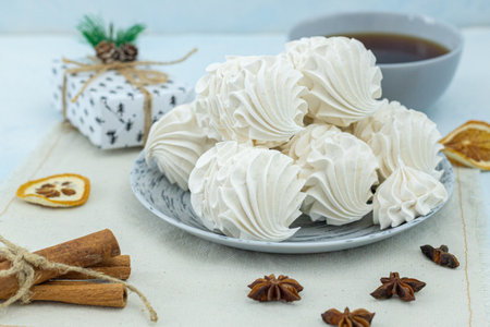 Meringue cookies displayed on a plate, with a cup of tea and seasonal decorations, creating a warm and inviting atmosphere for dessert loversの写真素材