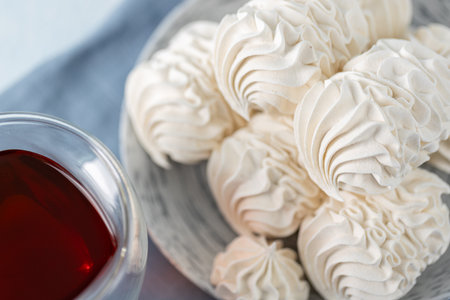 Meringue cookies beautifully arranged on a plate, with a glass of tea and decorative spices nearby, creating a warm and inviting dessert atmosphereの写真素材
