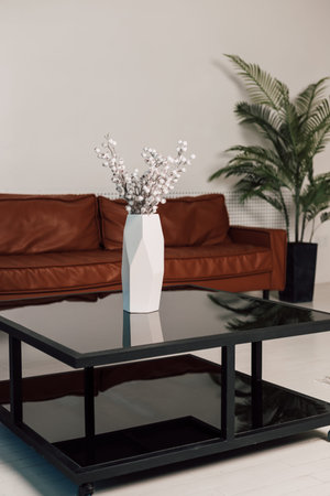 On a black glass table is a white vase of flowers in the office. High quality photo
