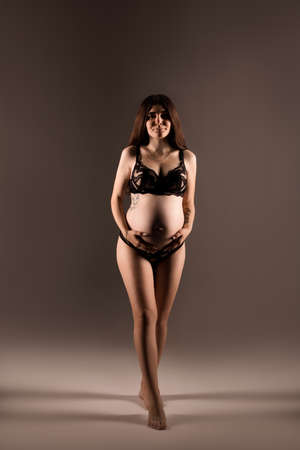 Pregnant woman in lingerie hugs her belly with her handsの写真素材