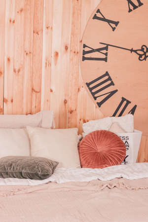 Pillows lie on a soft bed against the background of a wall clockの写真素材
