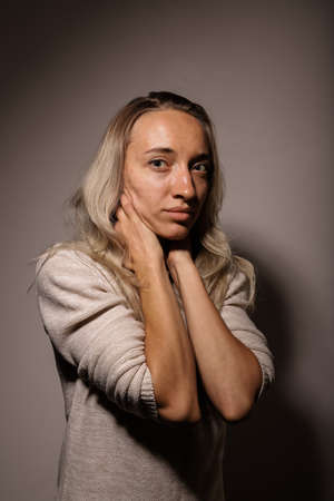 A young woman in grief with a sad face hugs her neck with her handsの写真素材