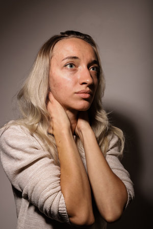 An upset girl stands in a dark room with her arms crossed against her face.の写真素材