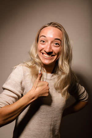 Funny young girl with blonde hair stands smiling and shows classの写真素材