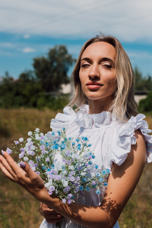 A young beautiful girl holds flowers in her hands and smilesの写真素材