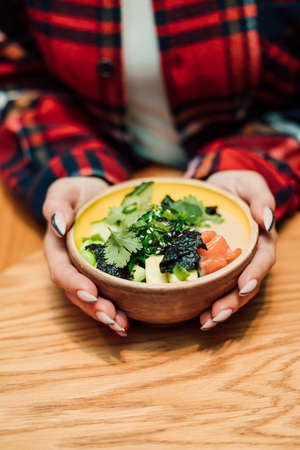 Delicious salad of tomatoes and greens in a deep plate and hands of a womanの写真素材