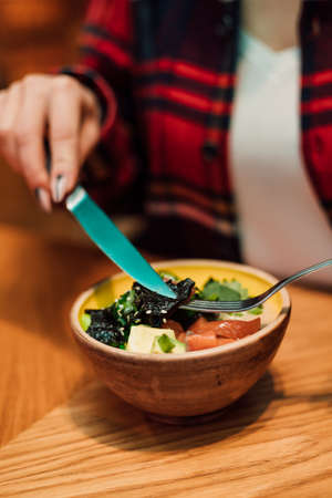 In the hands of a woman a knife and a fork over a plate of vegan saladの写真素材