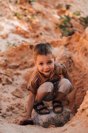 A little boy sits in the sand playing with a small carの写真素材
