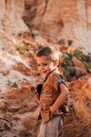 A little boy stands in the middle of the sand and holding a toy in his hands