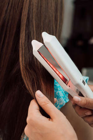 Hairdresser evens out the clients brown hair with a curlerの写真素材