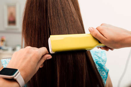Hairdresser evens out the clients brown hair with a curlerの写真素材