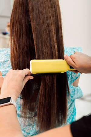 Hairdresser evens out the clients brown hair with a curlerの写真素材