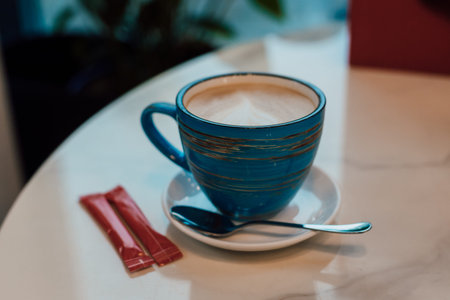 A cup of cappuccino on a saucer stands in a cafe on a table near the window