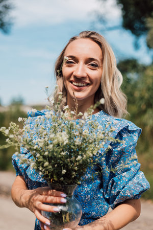 A young beautiful woman in a blue dress holds wild flowers in her handsの写真素材