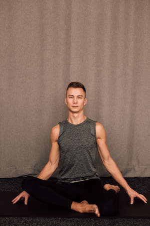 Young handsome athlete sits in the lotus position indoorsの写真素材