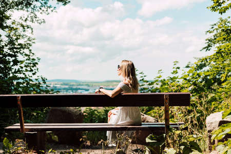 A woman sits with her back on a bench and looks at the city and the mountainsの写真素材