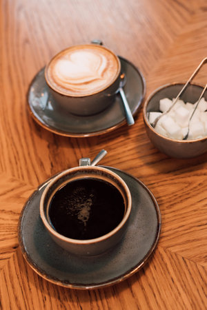 A cup of coffee, refined sugar and cappuccino on a wooden table
