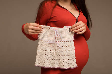 A pregnant woman holds in her hands a childs dressの写真素材