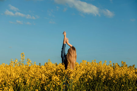 A girl in a rapeseed field stands with her back at sunset