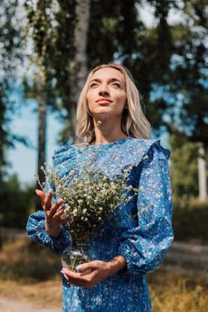 A young beautiful woman in a blue dress holds wild flowers in her handsの写真素材