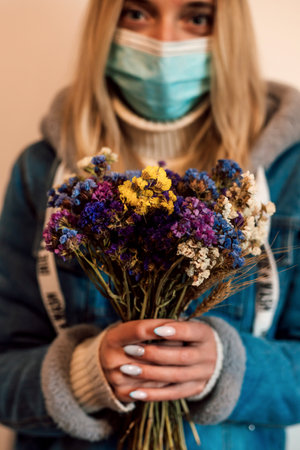 A young woman in a medical mask holds dried flowers in her handsの写真素材