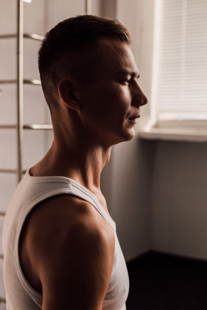 A young athlete in a white T-shirt sits near the windowの写真素材