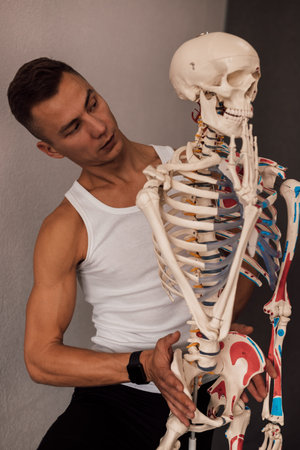 A man in a white T-shirt studies the structure of the human skeleton