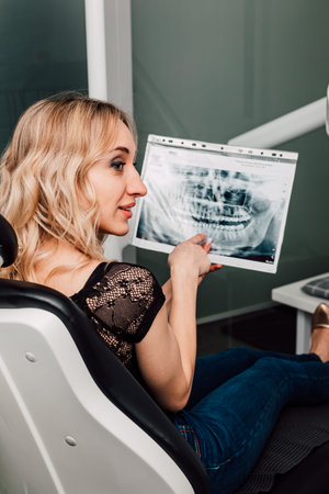 The patient sits in the dentists chair and holds an X-ray of the teeth