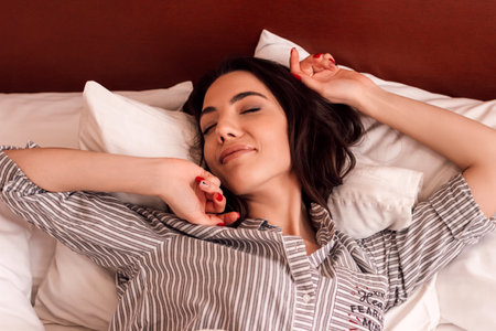 A young beautiful girl sleeps with a teddy bear in a bed in pajamasの写真素材