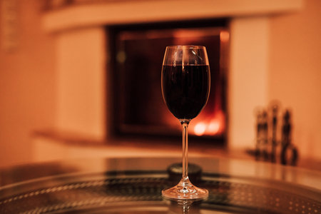 A glass of red wine on a glass table near the fireplace. Christmas Eveの写真素材
