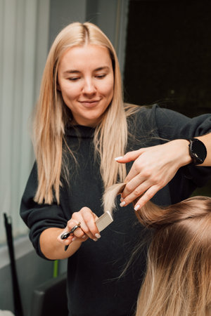 A hairdresser cuts a blondes hair in a beauty salon. Womens haircut