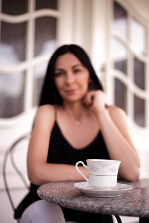 Attractive woman with a cup of coffee sitting at a table on the streetの写真素材