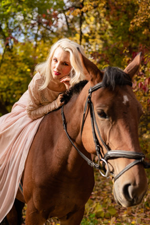 A woman in a long dress sits on a horse. Autumn forest, horse breedingの写真素材